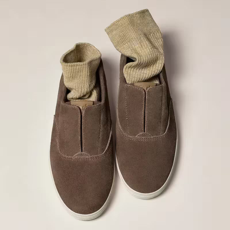 A pair of the Keds Champion Round Toe Suede Slip-On in cocoa brown with oatmeal-colored socks tucked in.
